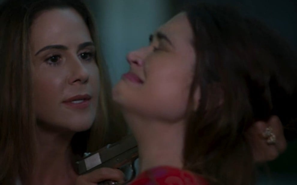 A atriz Guilhermina Guinle aponta uma arma no rosto da atriz Juliana Paiva (com cara de choro e desespero) em cena como Luna de Salve-se Quem Puder