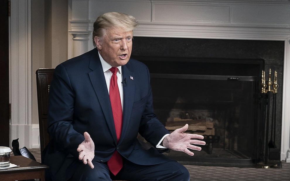 O presidente dos Estados Unidos Donald Trump sentado em uma cadeira com um terno azul e uma gravata vermelha