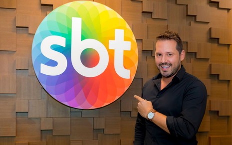 Dony De Nuccio posa sorridente ao lado do logotipo do SBT