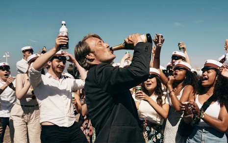 Mads Mikkelsen bebe champanhe em cena de Druk: Mais Uma Rodada