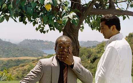 Eddie Murphy como Jack McCall vestido com terno marrom claro, com a mão tampando boca e Cliff Curtis como Dr. Sinja vestido de branco