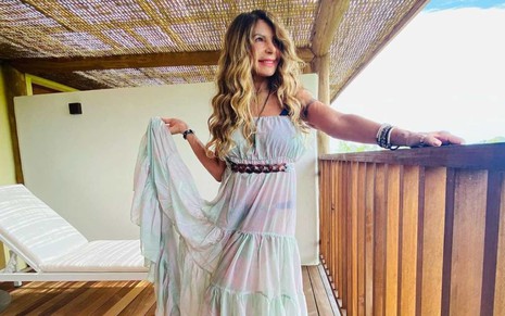A cantora Elba Ramalho de vestido branco, olha para o lado com mão em corrimão de madeira em varanda de sua casa