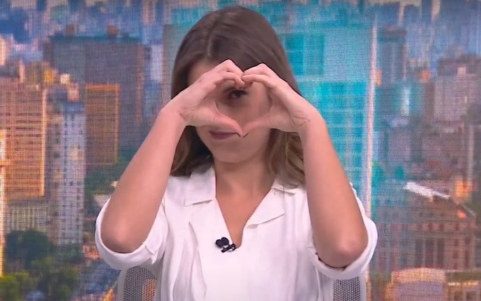 A jornalista Elisa Veeck, com camisa social branca, aparece fazendo coraçãozinho com a mão no CNN Novo Dia