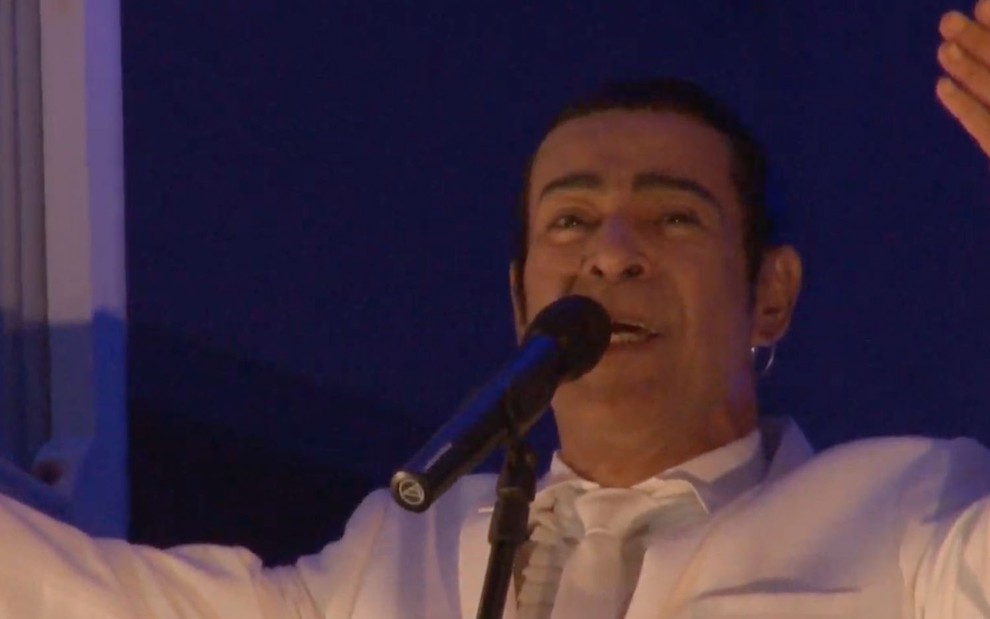 O cantor Elymar Santos em frente a um microfone com os braços abertos
