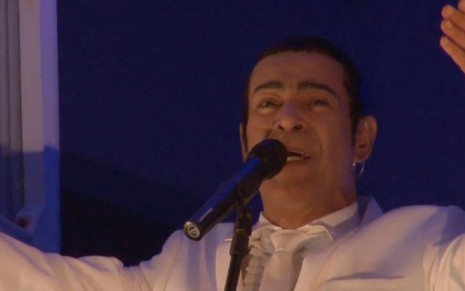 O cantor Elymar Santos em frente a um microfone com os braços abertos
