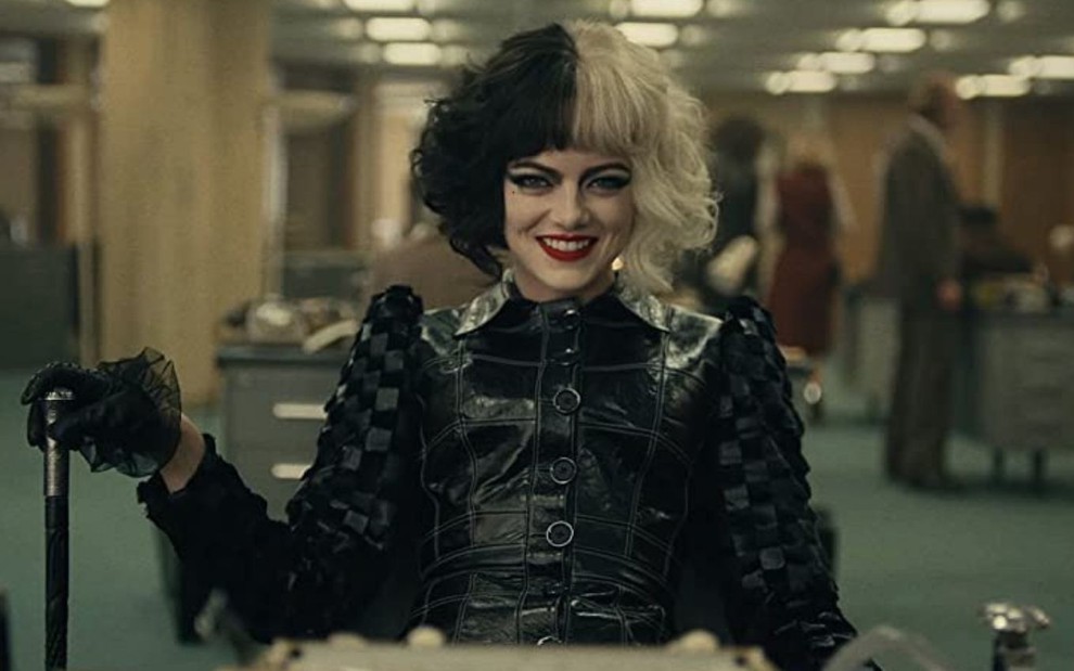 Emma Stone caracterizada como a vilã Cruella no live-action da Disney; ela usa um cabelo metade preto metade platinado e sorri maliciosamente