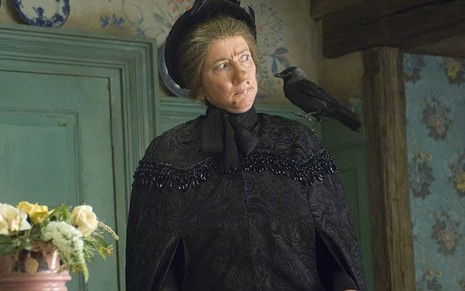 A atriz Emma Thompson vestida toda de preto e com um corvo no ombro em cena de Nanny McPhee e as Lições Mágicas (2010)