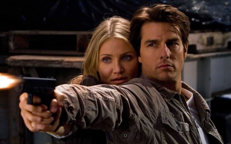 Cameron Diaz junto de Tom Cruise; os dois estão com as mãos unidas apontando uma arma