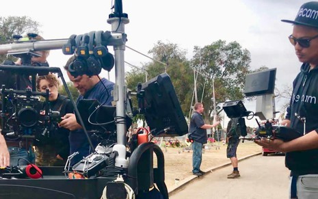 De boné e óculos escuro, operador de câmera mexe em um aparelho que controla um drone nos bastidores da série Vida