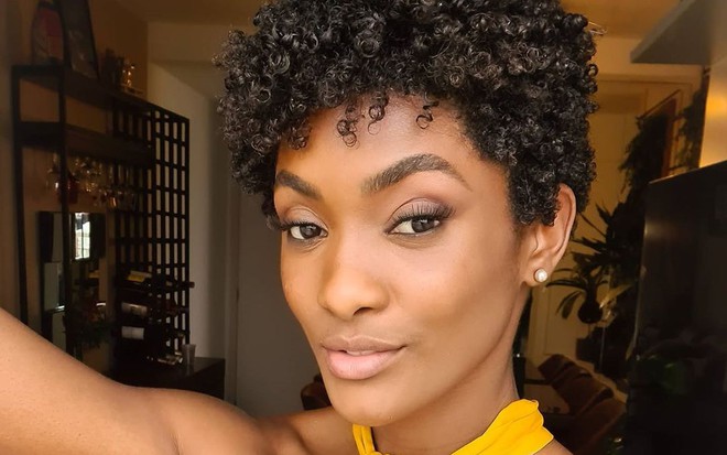 Erika Januza fazendo carão em selfie com o cabelo crespo curtinho e blusa amarela