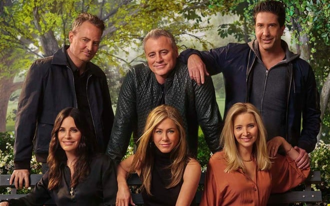 Matthew Perry, Matt LeBlanc e David Schwimmer na parte de trás de um banco e Courteney Cox, Jennifer Aniston e Lisa Kudrow sentada no banco em cenário florido