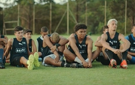 Meninos de 16 a 19 anos sentados no gramado de um campo de futebol