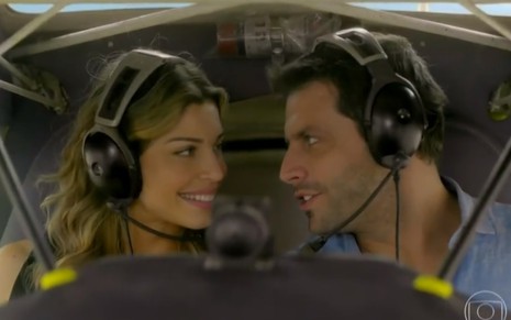 Grazi Massafera e Henri Castelli sorrindo e se olhando dentro de um helicóptero em cena de Flor do Caribe
