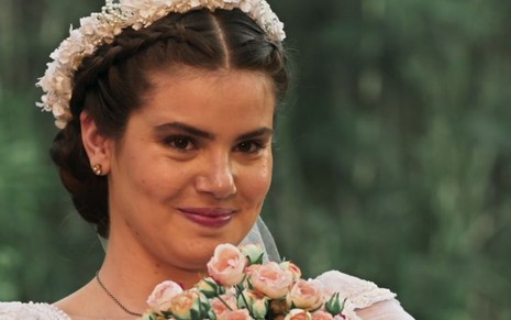 Vestida de noiva e segurando um buquê, Mafalda (Camila Queiroz) sorri em cena de casamento de Êta Mundo Bom!