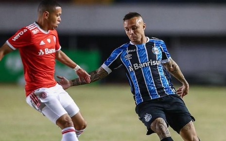 Imagem exibe um jogador do Grêmio e outro do Inter em disputa de bola