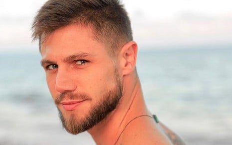 Jonas Sulzbach sem camisa, de barba, em foto tirada na praia