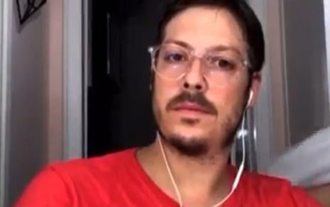 Fábio Porchat com o olhar sério, vestindo uma camiseta vermelha, durante live com Guilherme Boulos