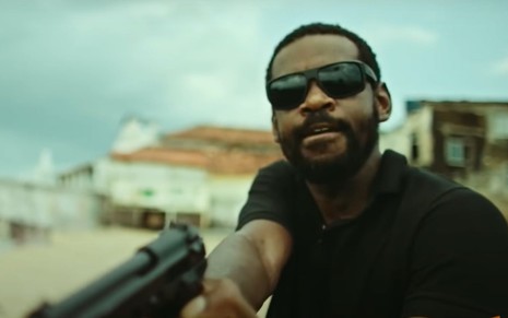 Fabrício Boliveira aponta uma arma para frente em cena do filme Tungstênio (2018)