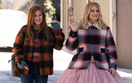 Com roupas de inverno, Isla Fisher e Jillian Bell acenam para alguém em cena do filme Fada Madrinha (2020)