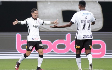 Os jogadores do Corinthians, Fagner e Jô comemoram o gol do time, um de frente para o outro, ambos de braços abertos, vestido com o uniforme do time nas cores branco e preto