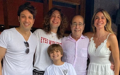 Luciana Gimenez posa ao lado do pai, do filho e do irmão, todos estão com roupas brancas e abraçados; outro filho de Luciana está perto de Lucas Jagger e também veste camiseta branca