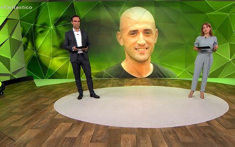 Tadeu Schmidt e Poliana Abritta no cenário do Fantástico com a foto de Paulo Gustavo em fundo verde
