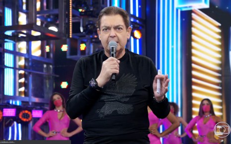 Apresentador Fausto Silva nos estúdios da Globo, vestido de preto e com um microfone na mão