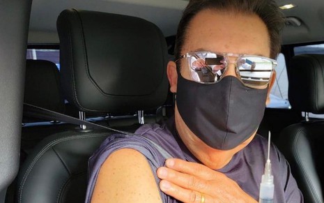 Com óculos escuros e máscara, Fausto Silva mostra o braça para receber vacina contra a Covid-19