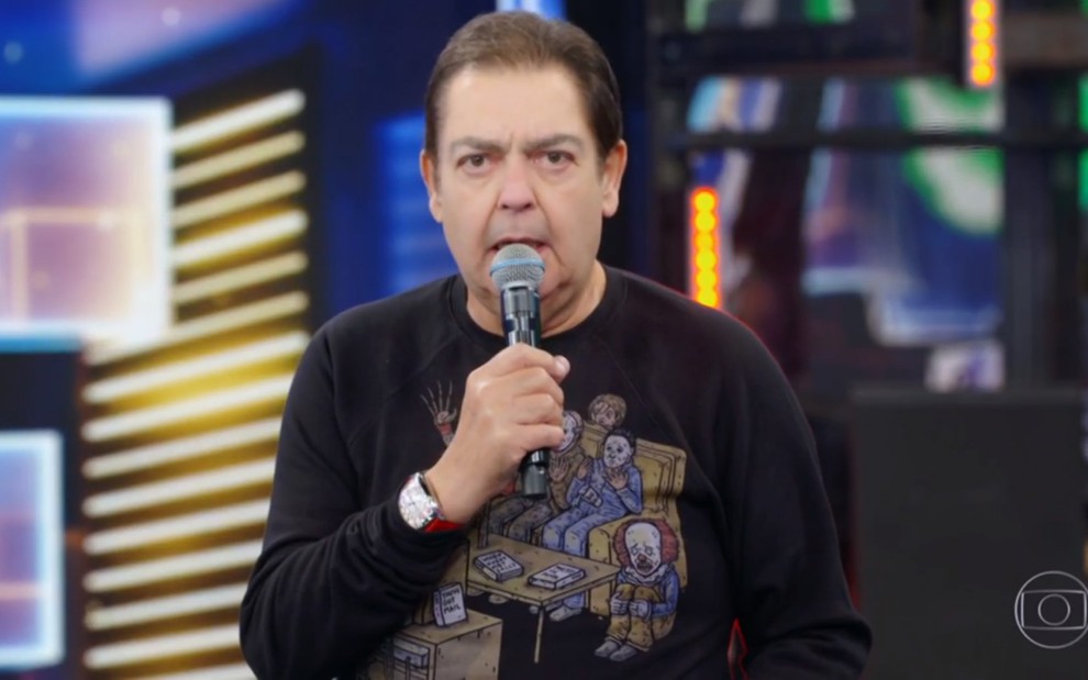 Fausto Silva segurando um microfone e vestindo uma camiseta de manga longa preta