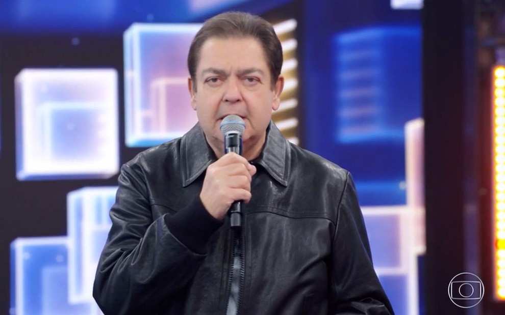 O apresentador Fausto Silva no Domingão do Faustão; ele veste jaqueta preta e está à frente de cenário luminoso