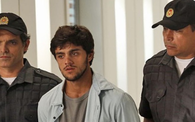 O ator Felipe Simas (Jonatas) algemado e com expressão de choro enquanto é conduzido por dois policiais