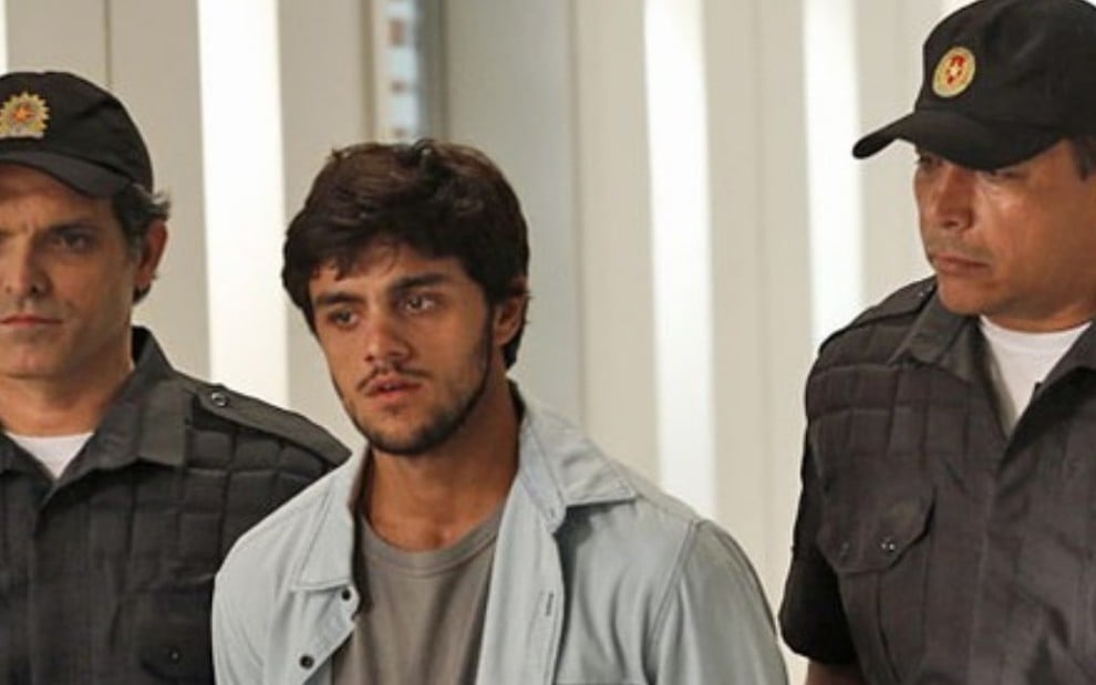 O ator Felipe Simas (Jonatas) algemado e com expressão de choro enquanto é conduzido por dois policiais