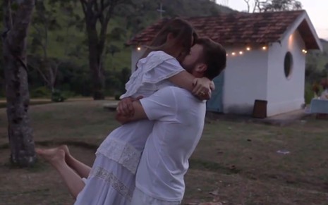 O casal Fernanda Lima e Rodrigo Hilbert abraçados em frente à capela construída no sítio da família