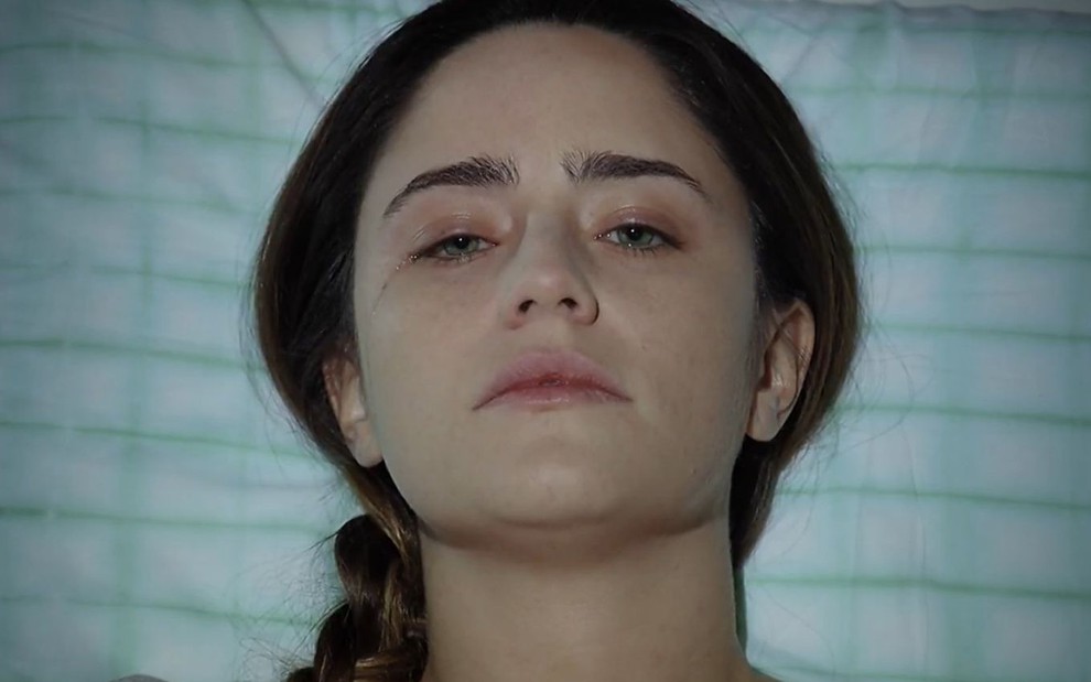A atriz Fernanda Vasconcellos deitada em uma cama de hospital com os olhos quase abertos em cena como Ana de A Vida da Gente
