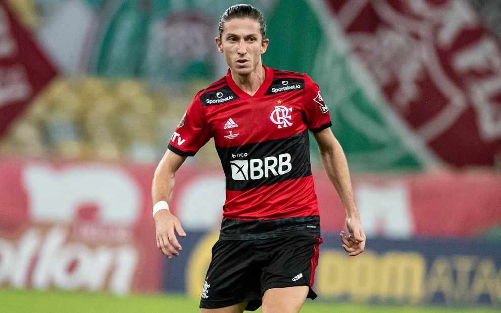 Flipe Luís com o uniforme preto e vermelho do Flamengo com olhar atento para a direita com detalhes desfocados do estádio ao fundo