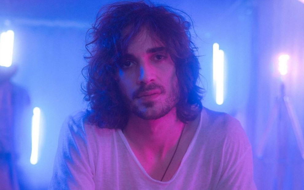 Imagem de Fiuk iluminado com luzes roxas com fundo azul nos bastidores do clipe Amor da Minha Vida