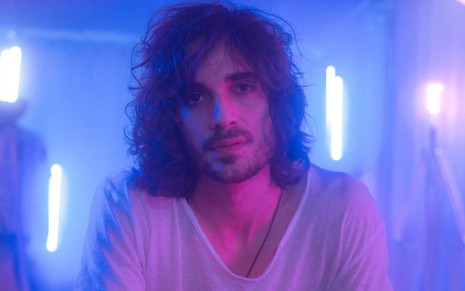 Imagem de Fiuk iluminado com luzes roxas com fundo azul nos bastidores do clipe Amor da Minha Vida