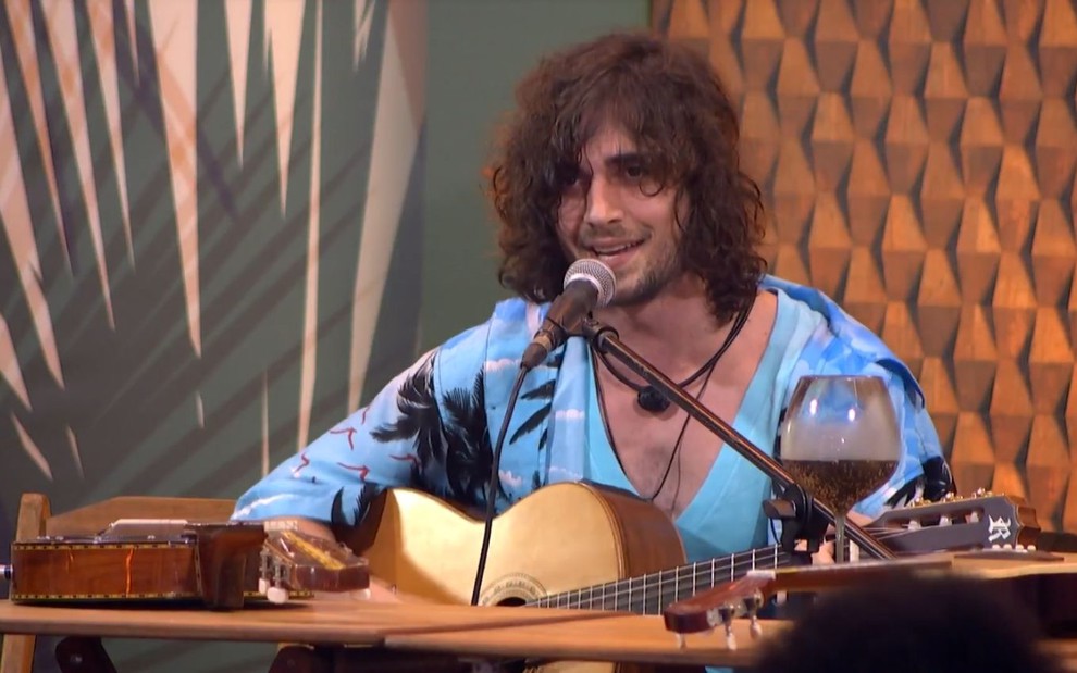 O cantor Fiuk usa uma camisa azul clara estampada enquanto toca violão e canta em um microfone no BBB21