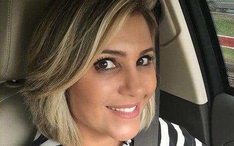 Flávia Freire sorridente, de cabelo curto com luzes, dentro do carro com blusa listrada de preto e branco