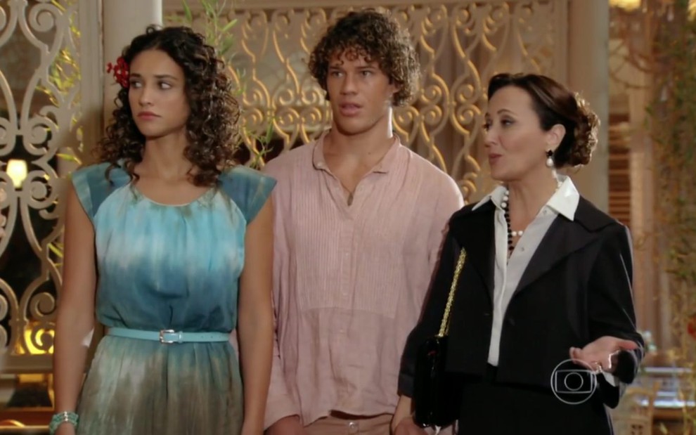 Os atores Débora Nascimento, Jospe Loreto e Claudia Netto lado a lado em cena de Flor do Caribe; Claudia fala, Débora e Loreto têm olhares apreensivos