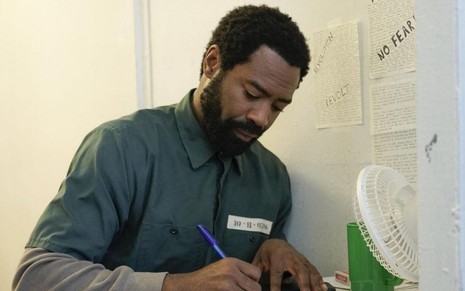 Dentro de uma cela, o ator Nicholas Pinnock escreve em um bloco de notas durante cena de For Life