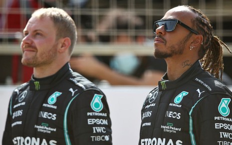 Valtteri Bottas e Lewis Hamilton olham para o alto vestidos com o uniforme da Mercedes