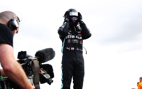 Lewis Hamilton sobe no carro e coloca as mãos sobre o capacete para comemorar vitória na Fórmula 1
