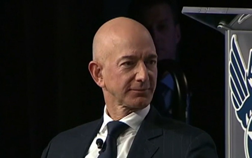 Jeff Bezos, de terno e gravata, tem expressão séria em entrevista