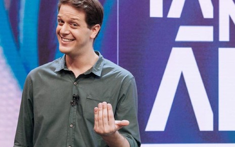O jornalista Fred Ring de camisa verde escura, sorri no cenário do programa Tá na Área, do SporTV
