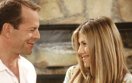 Os atores Bruce Willis e Jennifer Aniston sorriem um para o outro em cena da comédia Friends
