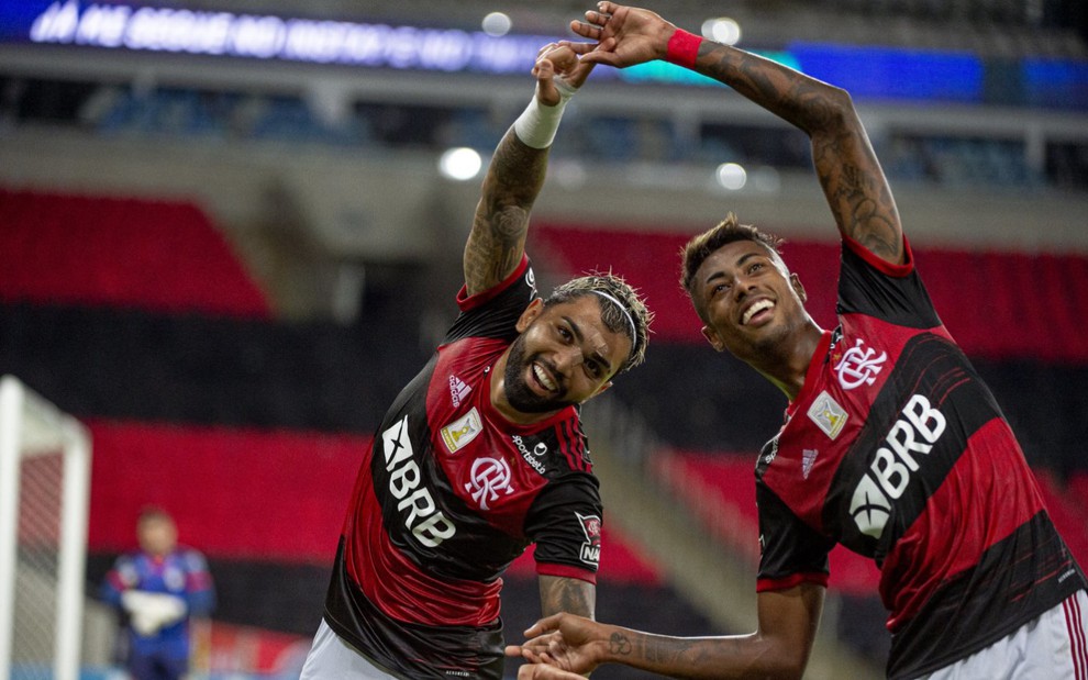 Gabigol e Bruno Henrique vestidos com tradicional uniforme do Flamengo nas cores vermelha e preta, unem as mãos formado um algo parecido com um círculo