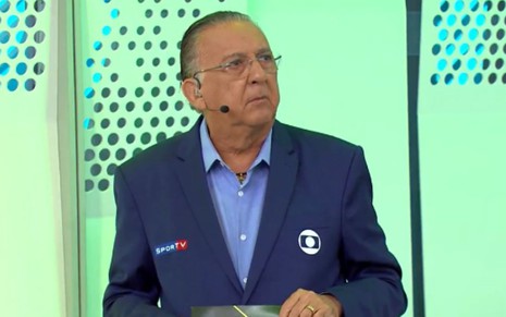 Galvão Bueno em transmissão do futebol da Globo, de terno azul marinho, olhando para o lado esquerdo