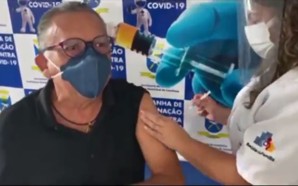 Galvão Bueno com manga levantada, máscara e óculos, recebe a vacina de profissional da saúde