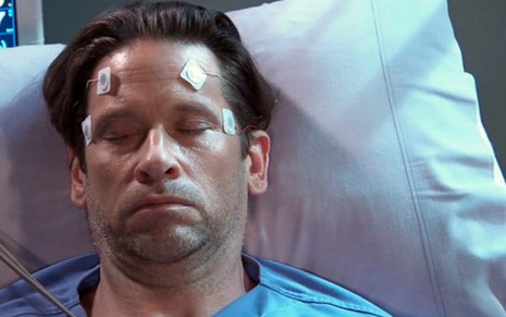 O ator Roger Howarth em um leito hospitalar, de olhos fechados, em cena da novela americana General Hospital